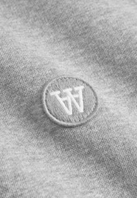 Gray fabric with a smooth texture featuring a circular embroidered logo of two letters “W” in white, centered on the material.