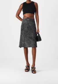 Schwarzes Crop-Top und grauer strukturierter Midi-Rock mit silbernen Hardware-Details. Kombiniert mit schwarzen Absatzsandalen mit Schnallenakzenten.