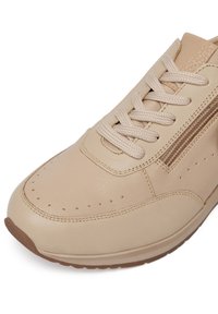 Bežid spordijalanid, millel on sile nahast pealispind ja perforeeritud detailid. Omab lapikuid paelu ja kummist tallat, millel on pruun aktsent.