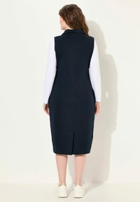 Abito senza maniche di colore blu navy con colletto, caratterizzato da uno spacco sul retro e una linea dritta, abbinato a sneakers bianche. Texture liscia, design casual.