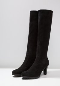 Bottes hautes jusqu'au genou en daim noir avec bout pointu, talon effilé et finition texturée. Aucune quincaillerie ni motif visible. Semelle à empreinte adhérente.