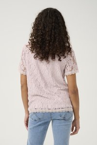 Top in pizzo rosa pastello con maniche corte e orlo in pizzo scallop, abbinato a jeans blu chiaro, che mette in mostra un motivo in pizzo aperto.