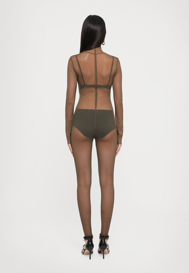 Doorzichtig bruin bodysuit met lange mouwen, met een aansluitend ontwerp en solide donkergroene shorts eronder. Zwarte hoge hakken worden gedragen.