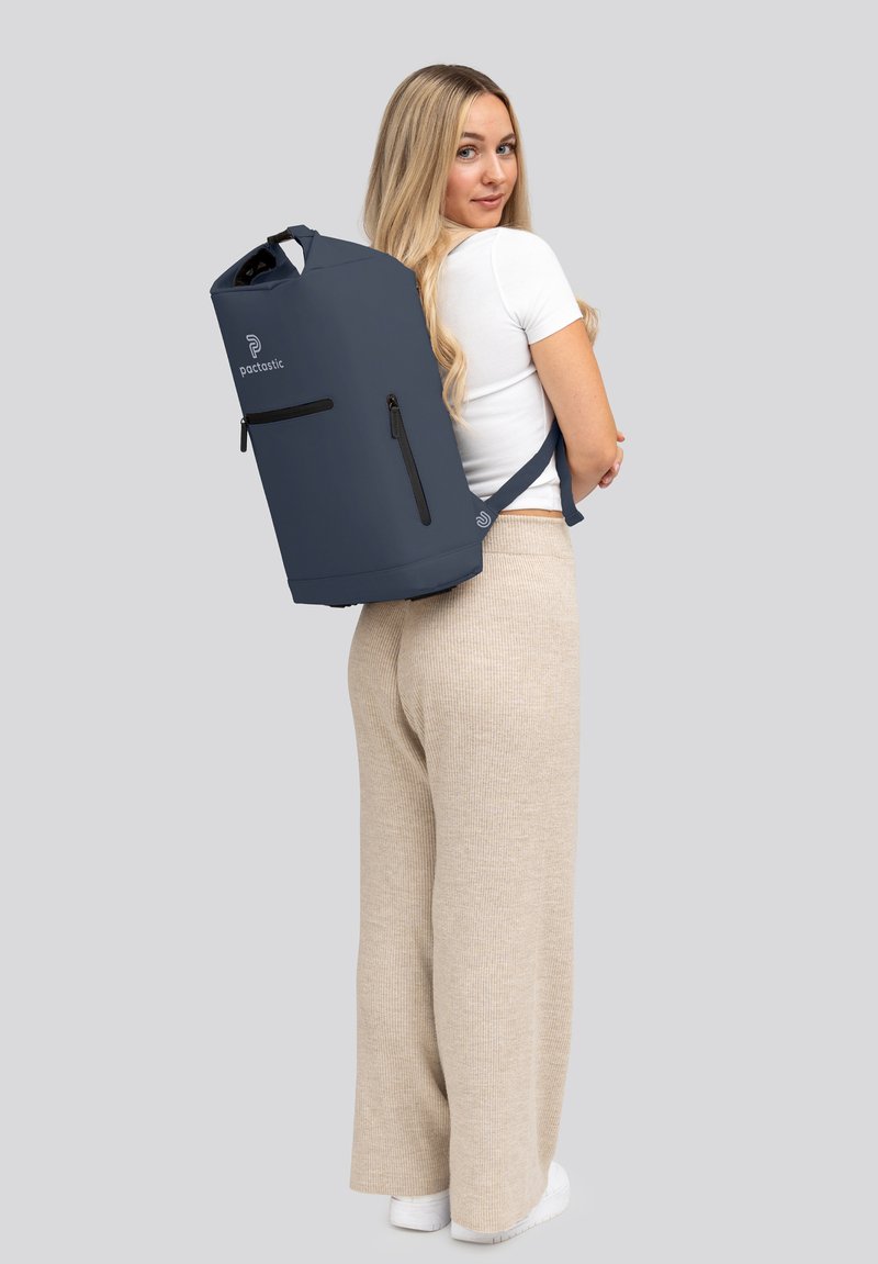 Mochila impermeable de color azul oscuro con cierre enrollable, bolsillo delantero con cremallera y correas ajustables; textura suave y minimalismo en la marca.