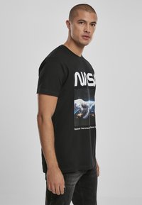 Černé bavlněné tričko s bílým logem "NASA" a potiskem grafiky rukou sahajících po Zemi s hvězdným pozadím.