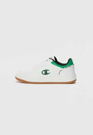 Hvide sneakers med grønne detaljer og sort foring, der har en tekstureret gummisål og broderet logo på siden.