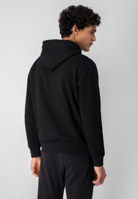 Sudadera negra hecha de un suave material de algodón, con capucha ajustable, puños acanalados y un corte relajado. Textura de tejido ligero.