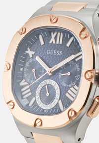 Montre en argent et or rose avec un cadran bleu à motifs, des index horaires en chiffres romains, des sous-cadrans et un bracelet en acier inoxydable.
