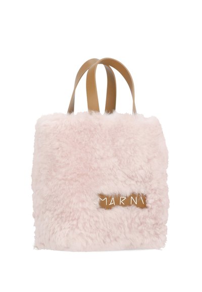 Borsa tote fluffy rosa con una consistenza morbida, dotata di manici in pelle beige e un'etichetta marrone con lettere bianche. Forma quadrata, design minimalista.