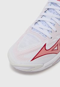 Άσπρο αθλητικό παπούτσι με κόκ�κινες λεπτομέρειες. Διαθέτει υφή από δίχτυ, καμπυλωτό σχεδιασμό και εμφανές σύστημα κορδονιών. Το λογότυπο της μάρκας εμφανίζεται ξεκάθαρα.