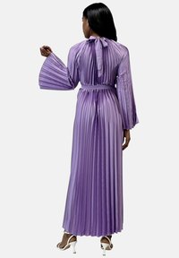 Lang, plisseret kjole i lyse lilla med bundet rygudskæring og klokkeærmer. Har et matchende bælte og en glat, flydende tekstur.
