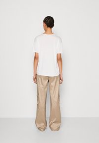 Biała koszulka z krótkim rękawem w połączeniu z jasnobeżowymi spodniami cargo o szerokich nogawkach, wykonanymi z gładkiego materiału, z bocznymi kieszeniami i luźnym krojem.