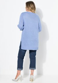 Světle modrý pletený cardigan s volným střihem, s ribedním lemem, postranními rozparky a měkkou texturou, doplněný o ohrnuté tmavé džíny.