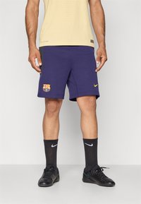 Tengeri kék bermuda, FC Barcelona logóval, puha anyagból készült. Fekete Nike zoknikkal és focicipőkkel párosítva. Világos sárga póló.