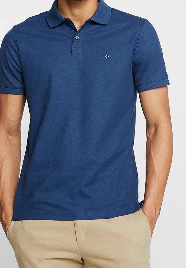 Homme portant un polo bleu ajusté à manches courtes avec un petit logo blanc sur la poitrine et un pantalon beige.
