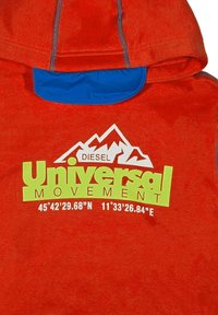 Felpa rossa con fodera interna blu, dotata del logo "DIESEL Universal Movement" in verde e coordinate geografiche stampate sotto.