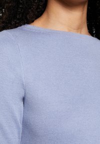 Ljusblå ribbad tröja med rundad halsringning, som har en texturerad tyg. Plagget har en mjuk finish och en figurnära silhuett.