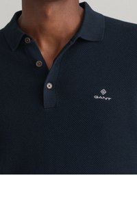 Dunkelblaues Polohemd aus strukturiertem Stoff, mit einer Zwei-Knopf-Leiste und GANT-Logo in Weiß auf der linken Brust.