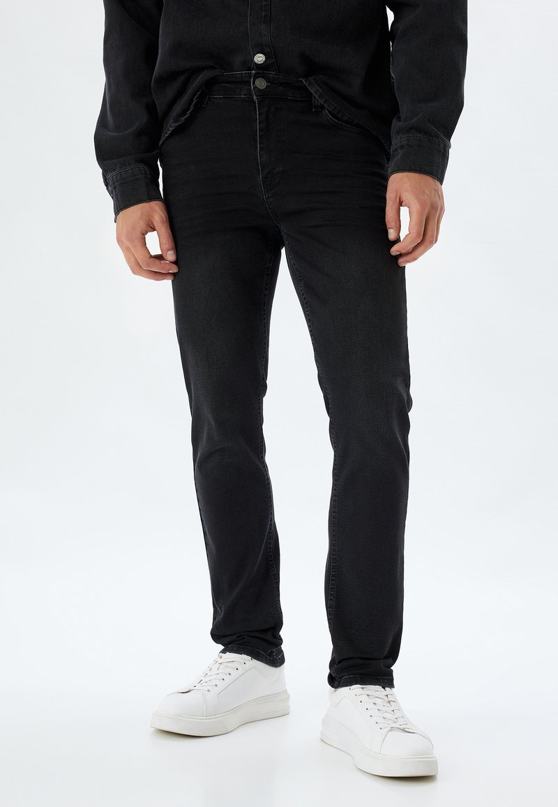 Czarne spodnie jeansowe slim-fit wykonane z denimu, z klasycznym pięciopocketowym fasonem, w połączeniu z białymi sneakersami.