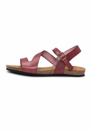 Sandalia de cuero rojo con plantilla de corcho, correa ajustable en el tobillo con hebilla de latón y suela plana negra vista de lado.