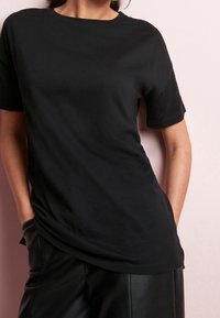 Sort bomulds t-shirt med rund halsudskæring og korte ærmer, parret med sorte læderbukser. Glat tekstur, afslappet pasform, synlig sidesøm.
