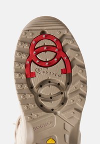 Beżowa podeszwa z gumy do kaloszy z czerwonym metalowym akcentem z kamieniami szlachetnymi oraz teksturowanym wzorem dla lepszej przyczepności. Nadrukowane napisy „Bogner” i „Q System”.