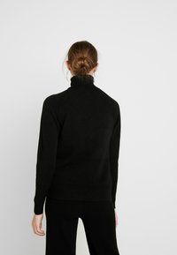 Černý svetr s rolákem a žebrovanými detaily, vyrobený z měkkého pleteného materiálu. Má dlouhé rukávy a přiléhavý střih.