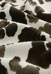 Multifarvet stof med et tekstureret mønster af brune og hvide kælvepletter, draperet i bløde bølger, der afslører dybde og detaljer.