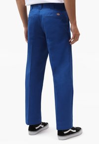 Modré bavlněné kalhoty s přímým střihem, se dvěma zadními kapsami a jemnými švovými detaily. Kombinovány s černo-bílými teniskami.