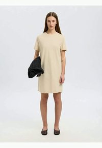 Beige short-sleeve dress with a straight shape. The model holds a black textured knitted item, wearing black flat shoes. Simple design.