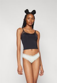 Schwarzes enges Top mit dünnen Trägern, kombiniert mit mintgrünen, spitzenverzogenen Unterhosen. Weiches, dehnbares Material mit glatter Textur.