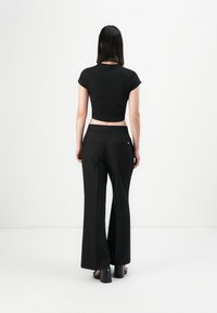 Black cropped t-shirt with cap sleeves paired with black wide-leg trousers. Trousers feature two back pockets and a smooth waistband.