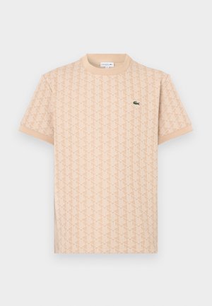 Bēša īsroku T-krekls ar ģeometrisku rakstu un zaļu Lacoste krokodila logotipu uz kreisās krūšu puses.