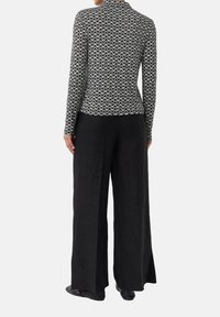 Long-sleeve top in black and white geometric print, paired with loose black pants. The top features a high neckline and fitted design.