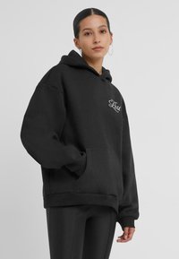 Hoodie oversize nero realizzato in tessuto morbido, con tasca frontale e testo ricamato "Lost" sul petto. Design semplice, vestibilità casual.