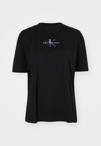 Crna pamučna majica s okruglim izrezom, koja sadrži istaknuti plavi i bijeli logo "Calvin Klein Jeans" preko prsa.