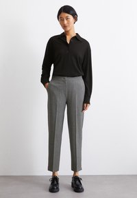 Cămașă polo neagră cu mânecă lungă și guler, asortată cu pantaloni drepți gri cu dungi și pantofi negri cu șiret.