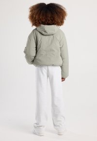 Giacca verde oliva imbottita con cappuccio, caratterizzata da spalle ribassate. Abbinata a pantaloni felpati grigi dalla vestibilità ampia e scarpe leggere.