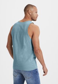 Light blue tank top made of soft fabric, featuring a round neckline and sleeveless design. Pairing with blue denim jeans.