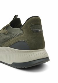 Talons de baskets vert olive avec tissu en suède et tricot, semelle intermédiaire beige texturée, semelle extérieure gris foncé, et petit logo BOSS sur la semelle.