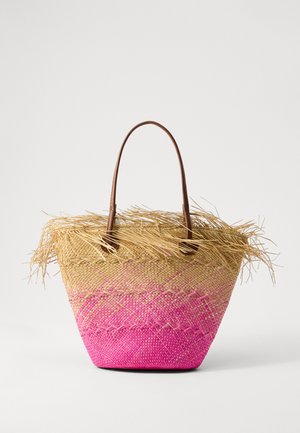 Sac fourre-tout en paille tissée avec des poignées en cuir marron, présentant un dégradé allant du beige au rose et des détails à franges sur le dessus. Surface texturée.