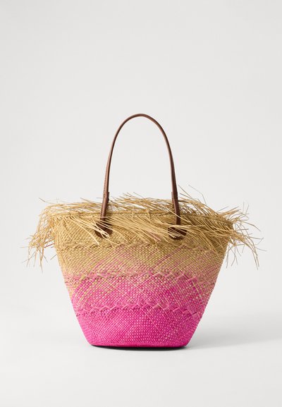 Sac fourre-tout en paille tissée avec des poignées en cuir marron, présentant un dégradé allant du beige au rose et des détails à franges sur le dessus. Surface texturée.