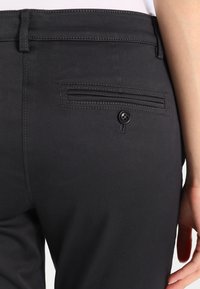 Czarne spodnie z tylną kieszenią zapinaną na guzik, gładką teksturą i subtelnym detalem przy pasku.