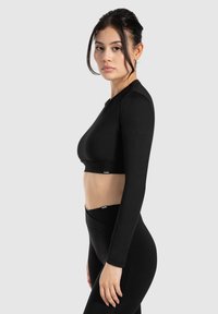 Schwarzes langärmeliges Crop-Top mit glatter Textur, entworfen für Sportbekleidung. Mit elastischem Bund am Saum, kombiniert mit passenden hochtaillierten Leggings.