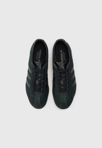 Pár černých tenisek Adidas s černými pruhy a tkaničkami, zobrazených zvrchu na bílém pozadí.