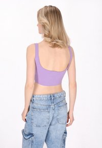 Top scurt violet cu un decolteu rotund și bretele groase, asortat cu blugi cargo de culoare albastră deschisă, cu talie înaltă și buzunare laterale.