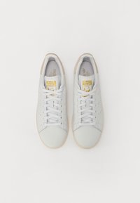 Zapatillas de cuero blanco con acentos texturizados, puntera redonda, cordones planos y una suela de goma beige. Presenta un logo dorado en la lengüeta.