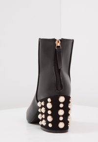 Schwarze Knöchelstiefel mit glattem Obermaterial, goldenen Reißverschluss und einem Blockabsatz mit Perlenakzenten. Verfügt über eine abgerundete Zehenpartie und einen schmalen Schaft.