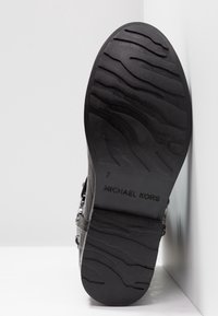 Semelle de botte noire avec un motif de bande de roulement ondulé, taille de chaussure 7, et "MICHAEL KORS" en relief au bas.