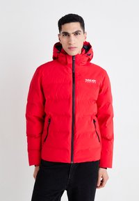Crvena puffer jakna s kapuljačom, sa prednjim zatvaračem, dva bočna džepa i logotipom. Glatka tekstura s kvadratnim uzorkom.